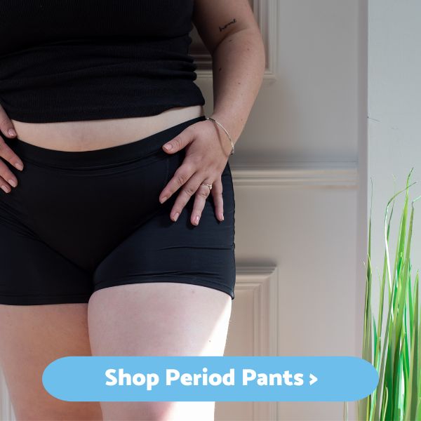 Lady wearing period shorts standing against a door. Button says 'shop period pants'